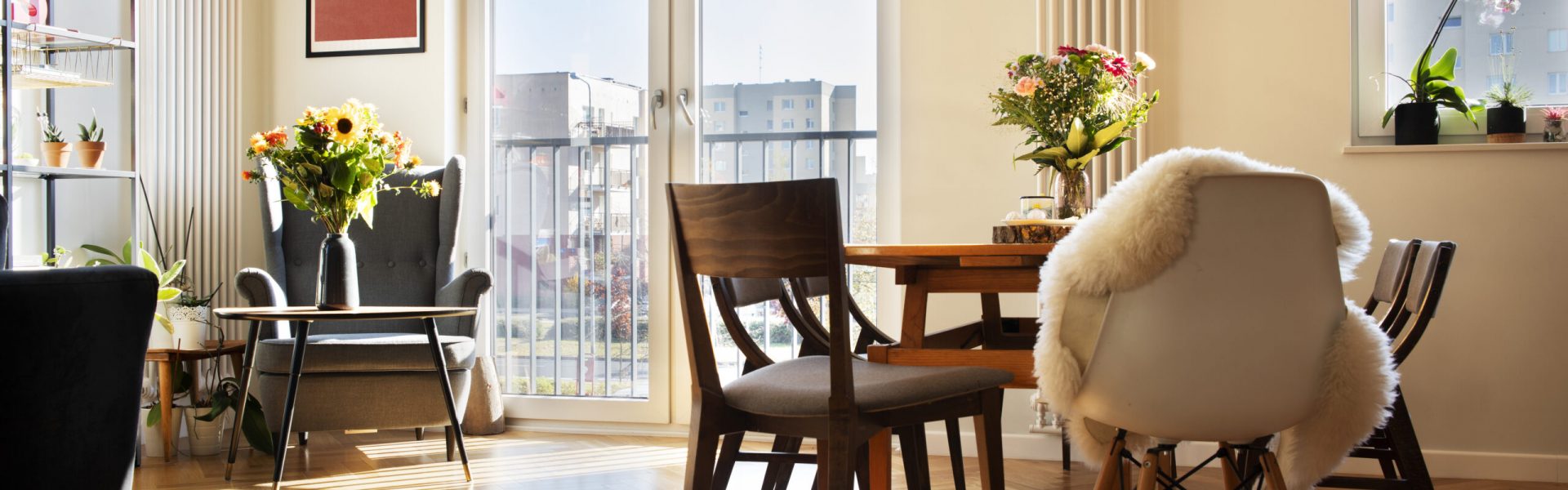 Stylish scandinavian open space interior of kitchen and dining room with design family table and chairs and other kitchen and dining room accessories. Bright and sunny room with big windows and brown wooden parquet.